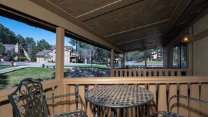 Un espace extérieur abrité, aménagé avec des chaises en métal et une table ronde, offrant une vue sur une zone verdoyante avec des bâtiments en arrière-plan.