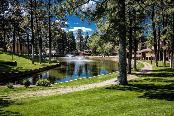 A tranquil hotel setting with a pond, lush greenery, and a clear sky. - Innsbrook Vacation Condo 1A (Ruidoso)