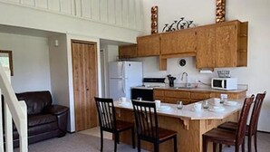 A compact kitchen with wooden cabinets, a refrigerator, a microwave, and a dining area with four chairs. - Crescent Bar Unit 102 (Quincy)