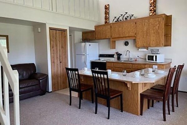 A compact kitchen with wooden cabinets, a refrigerator, a microwave, and a dining area with four chairs.