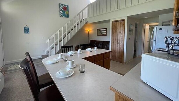A dining area with a long table set for four, a staircase, and a kitchen area with a refrigerator. - Crescent Bar Unit 102 (Quincy)