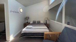 A bedroom with a bed, bedside tables, a lamp, a coat rack, and a window. - Crescent Bar Unit 102 (Quincy)