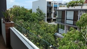 A balcony with a view of a modern building and surrounding greenery. - AC 1BR (Tulum)
