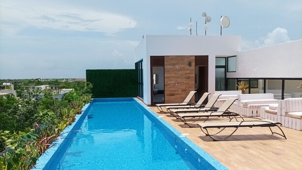 A rooftop swimming pool with lounge chairs and a modern building with large windows. - AC 1BR (Tulum)