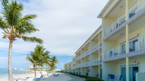 Un hotel frente a la playa con varios balcones, una playa de arena y palmeras.