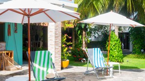 A patio area with two striped lounge chairs under white umbrellas, a hanging chair, and a small table. - Pousada Anauê (Conde)