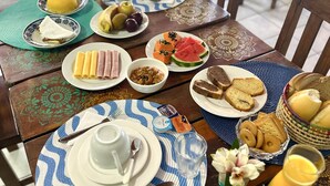 A dining table set with plates of food, including bread, fruits, and a drink. - Pousada Anauê (Conde)