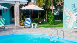A swimming pool with a clear blue water, surrounded by a tiled patio area with lounge chairs and umbrellas. - Pousada Anauê (Conde)