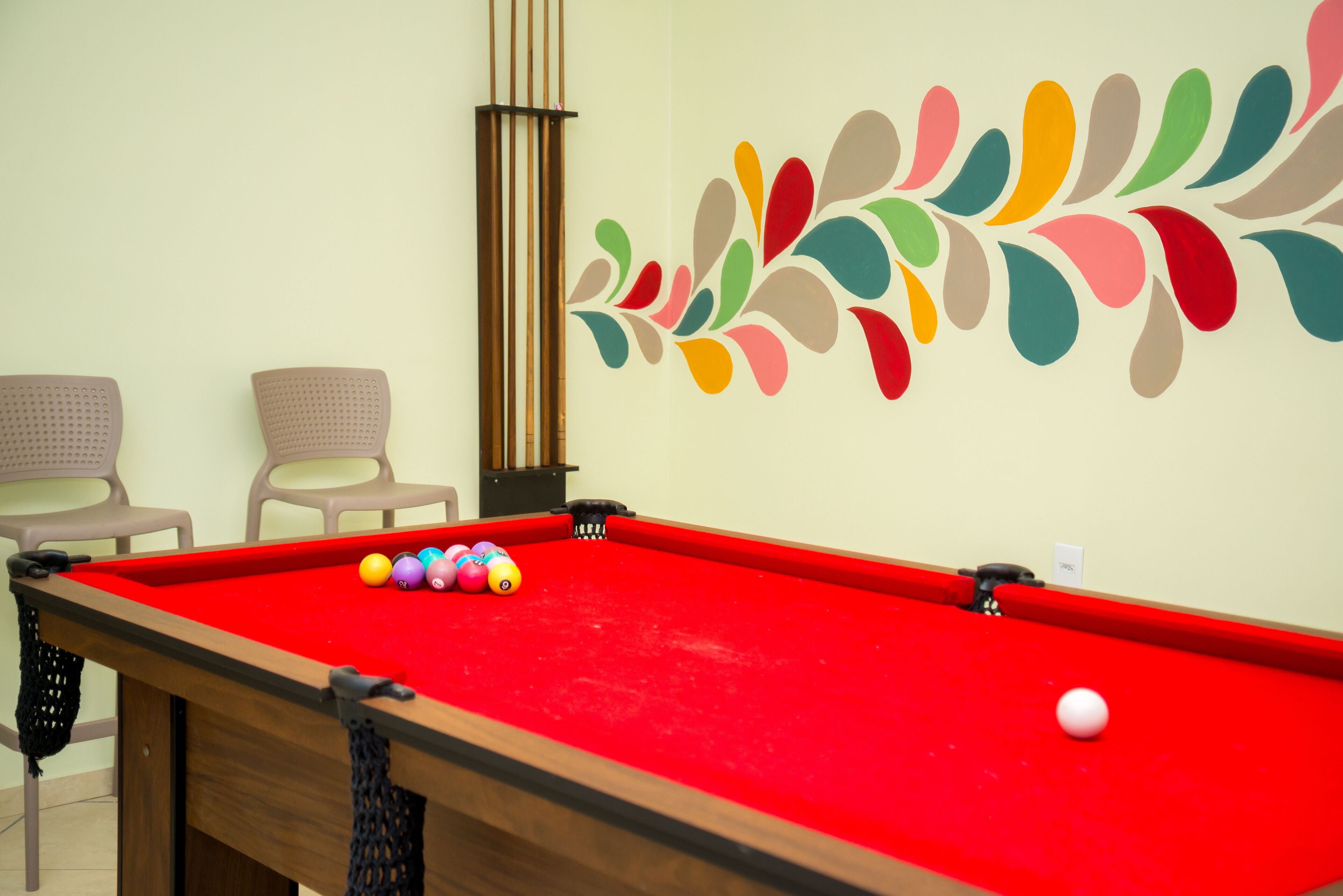 A pool table with balls, two chairs, and a decorative wall design.