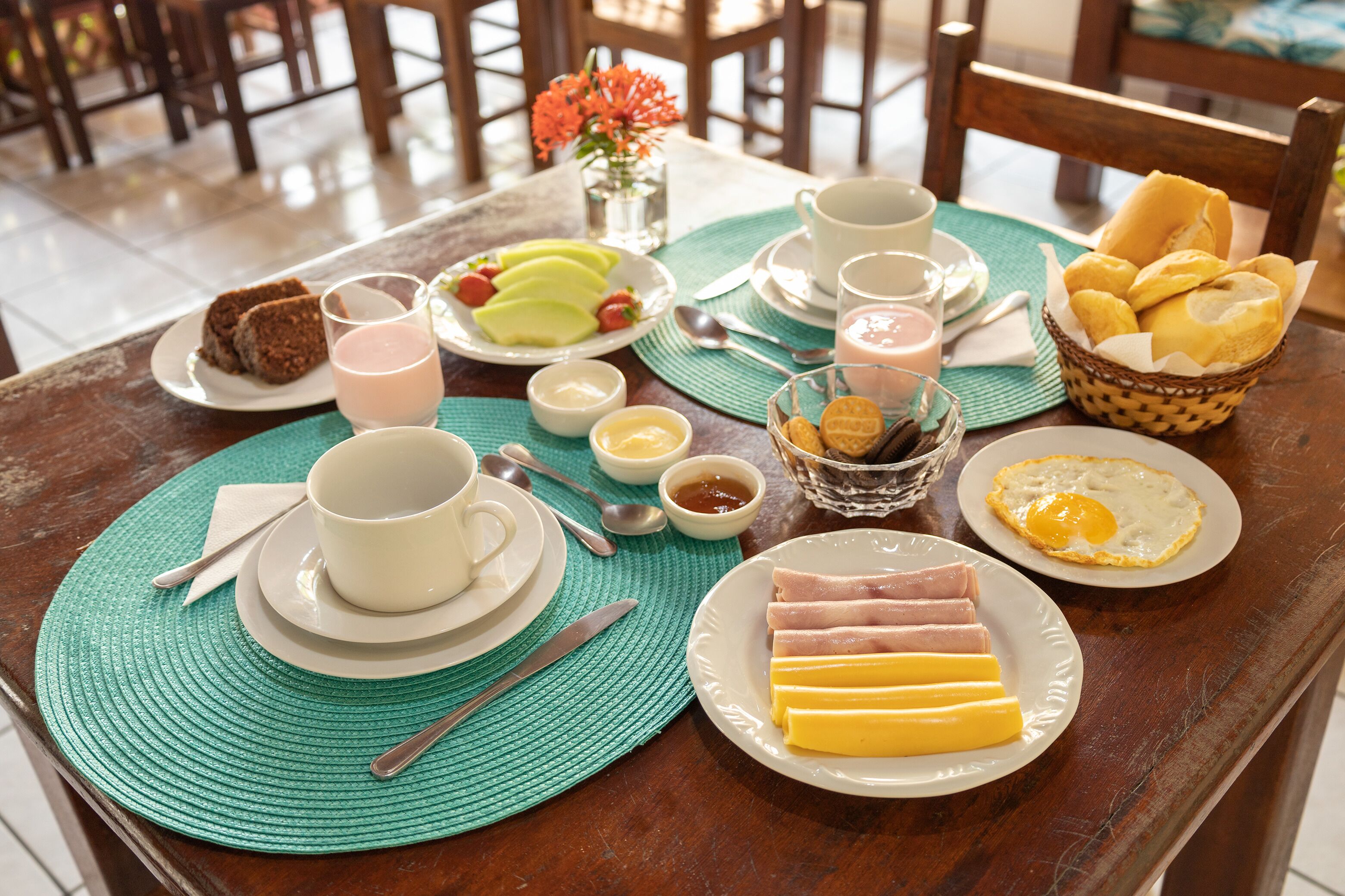 Una mesa de desayuno con platos de comida, tazas y un florero con flores.
