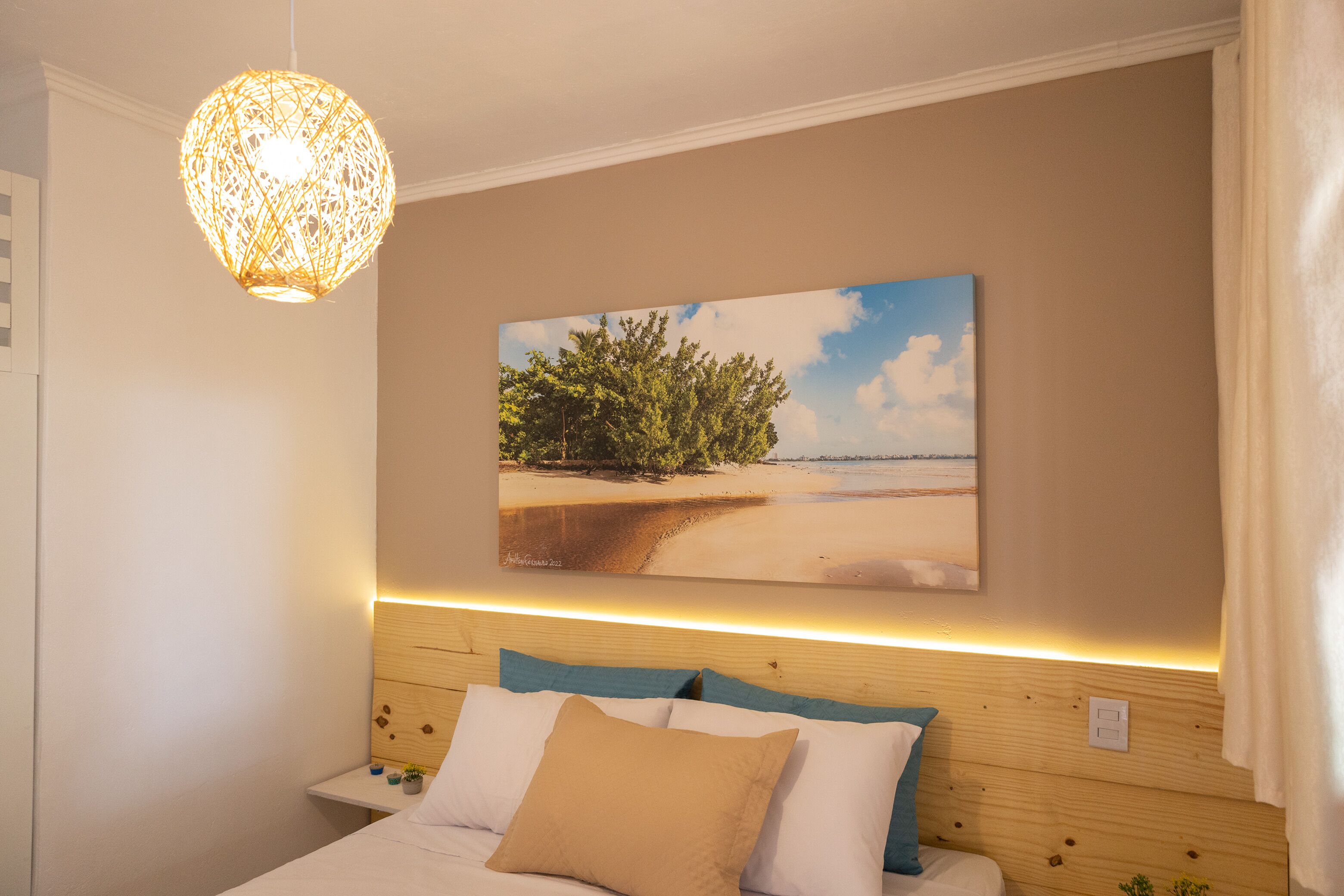 A bedroom with a wooden headboard, a painting of a beach, and a hanging light fixture.