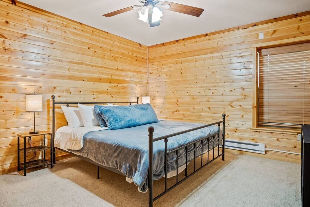A wooden-paneled bedroom with a bed, nightstands, and a ceiling fan.