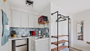 Una cocina compacta con armarios blancos, un microondas sobre una repisa de madera, un lavamanos y un refrigerador pequeño.