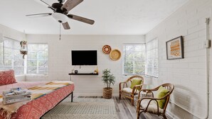 Un dormitorio con cama, televisor, sillas de mimbre y un ventilador de techo.
