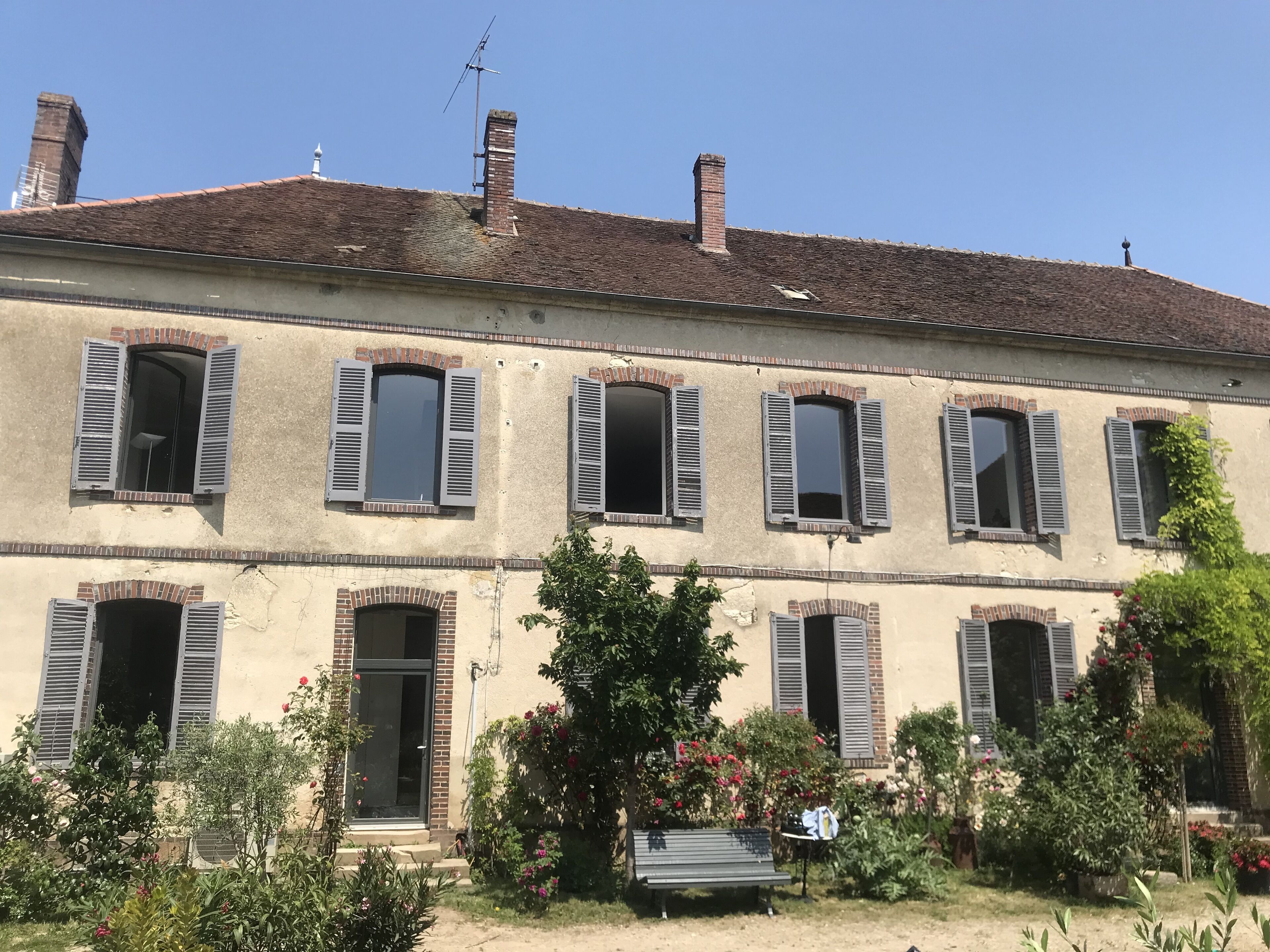 A two-story building with multiple windows, some with shutters, and a small garden area with a bench.