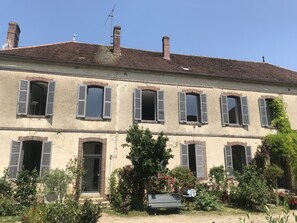A two-story building with multiple windows, some with shutters, and a small garden area with a bench.