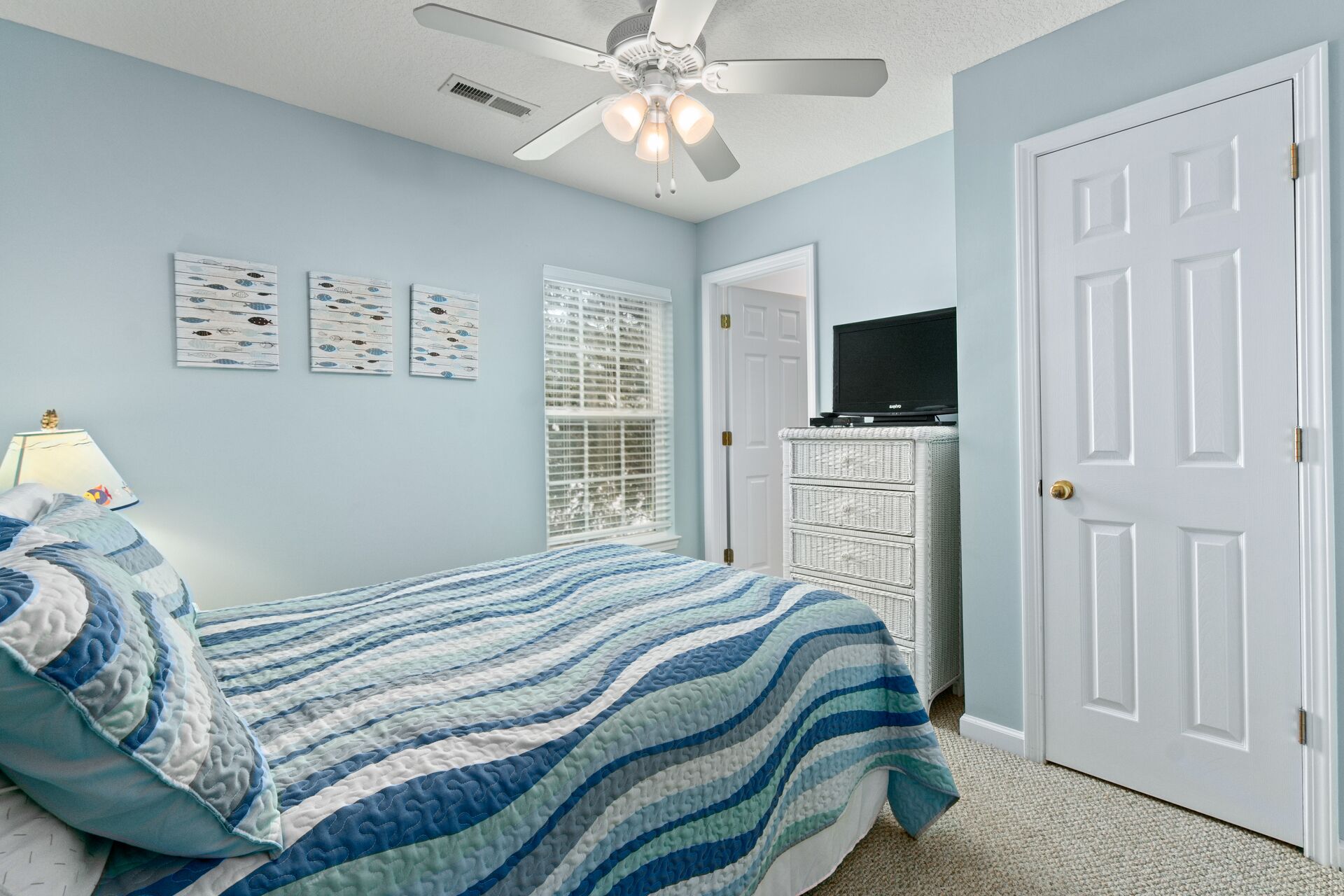 A bedroom with a bed, a ceiling fan, a television on a dresser, and a door.