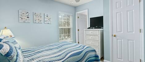 A bedroom with a bed, a ceiling fan, a television on a dresser, and a door.