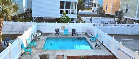 A backyard with a swimming pool, a wooden deck, and a white picket fence.