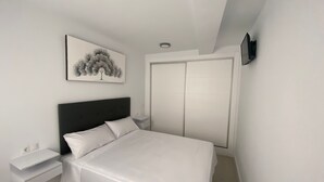 Un dormitorio con cama, mesita de noche, televisor en la pared y una puerta.