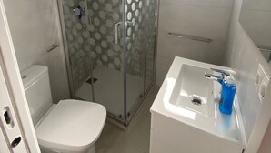 Un baño pequeño con ducha de vidrio, inodoro y lavamanos con dispensador de jabón.