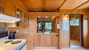 A wooden cabin kitchen with a stove, cabinets, and a dining area. - Happy Hideaway, short walk to Lake Huron (Bayfield)