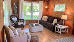 A cozy living room with wooden walls, a sofa, a chair, a coffee table, and a lamp.