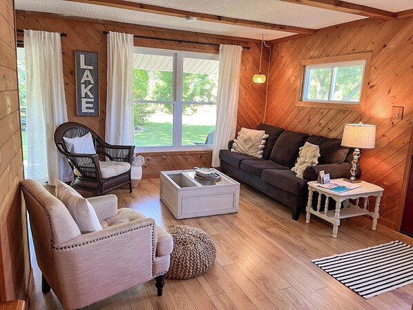 Een gezellige woonkamer met houten wanden, een bank, een fauteuil, een salontafel en een lamp.