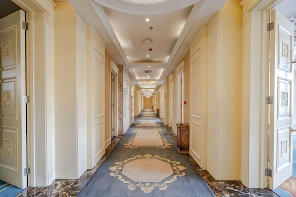 Un largo pasillo de hotel estrecho con puertas a ambos lados, una alfombra estampada y suelo de mármol.