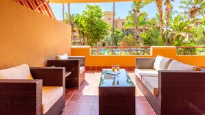 An outdoor seating area with wicker furniture and a glass table, overlooking a pool and greenery.