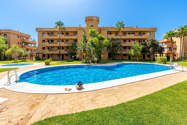 A hotel with a swimming pool, palm trees, and a clear blue sky.