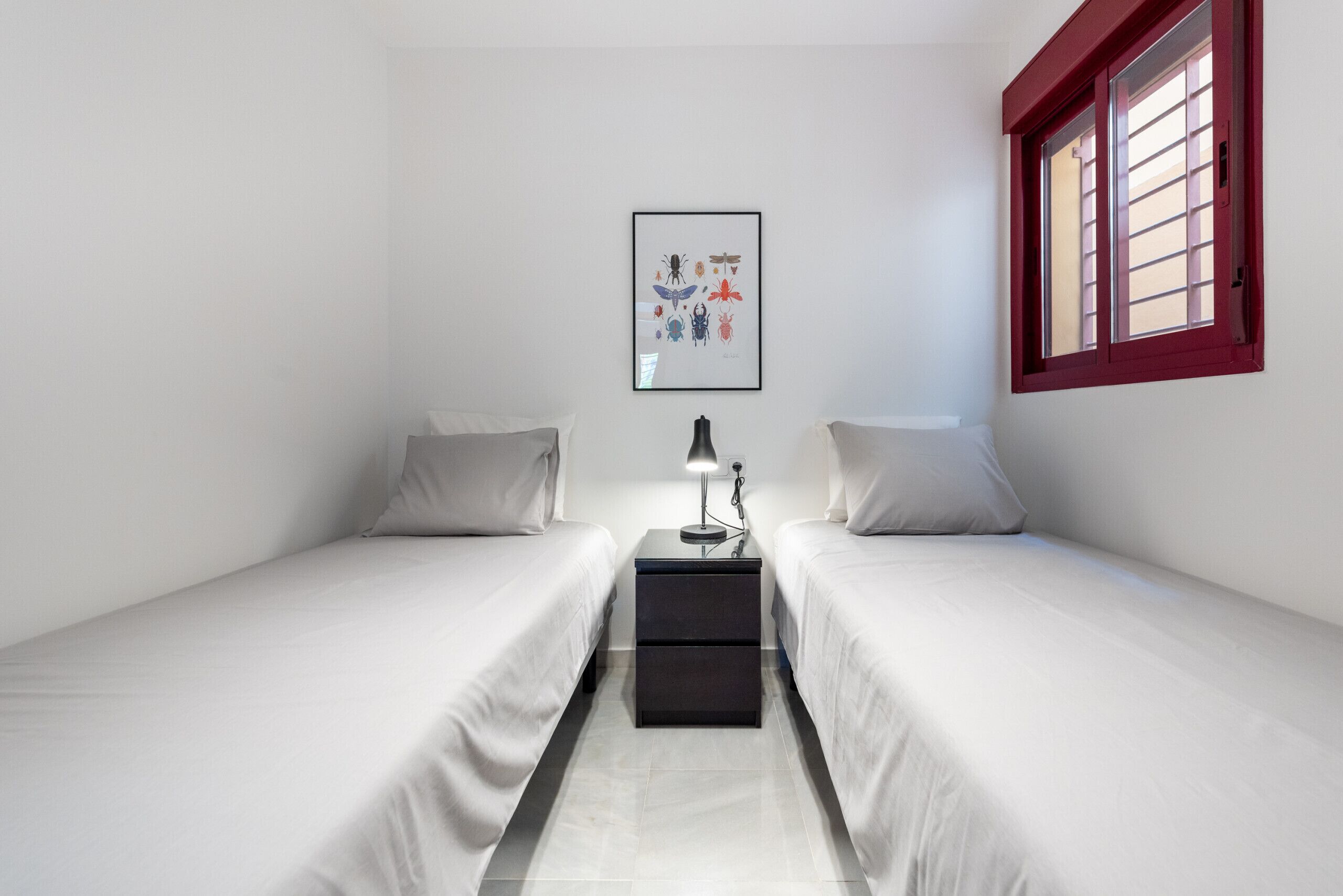 A small, clean room with two single beds, a nightstand with a lamp, and a framed picture on the wall.