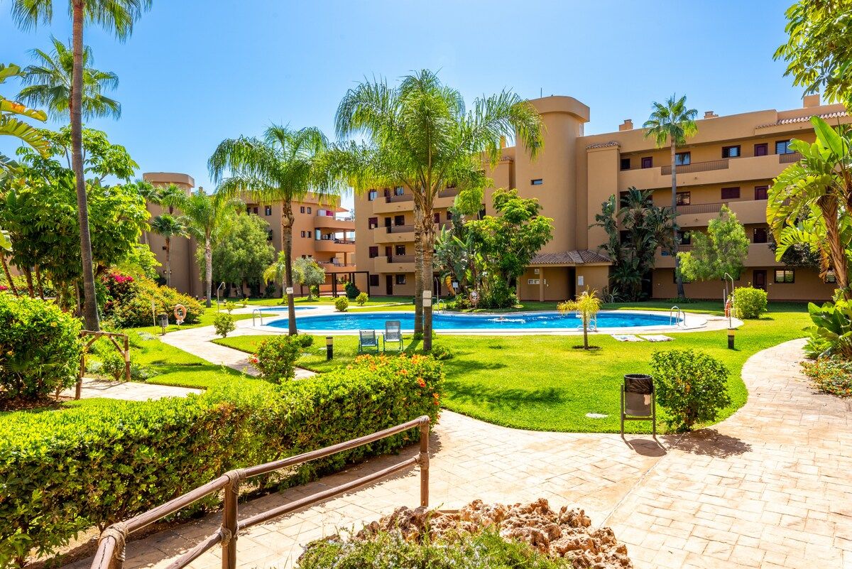 Une cour d’hôtel avec une piscine, des palmiers et une pelouse bien entretenue.