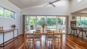 A spacious dining area with a wooden table and chairs, large windows, and a ceiling fan. - Frankie's Place ~ Stunning pet-friendly coastal home (CALLALA BEACH)