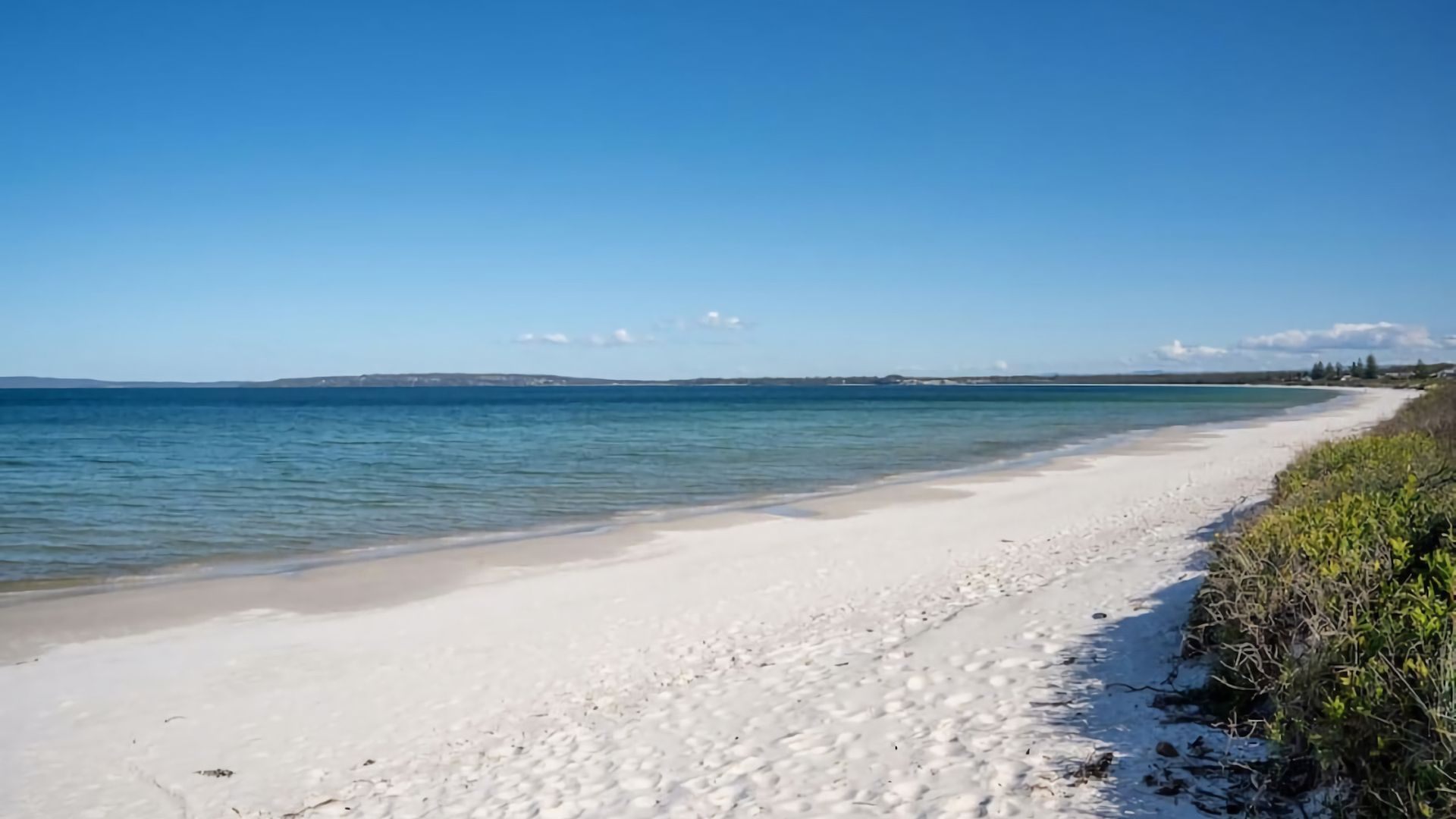 A beach with clear blue water and a sandy shore.