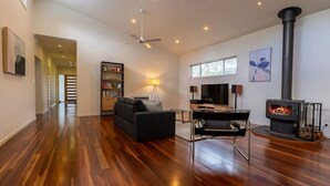 Ein geräumiges Wohnzimmer mit Holzdielenboden, einer Couch, einem Fernseher, einem Kamin und einem Bücherregal.