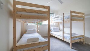 Een kamer met twee stapelbedden, elk voorzien van een matras en kussens, en een raam dat voor daglicht zorgt.