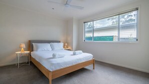 Une chambre à coucher avec un lit, deux lampes de chevet, un ventilateur de plafond et une fenêtre donnant sur un paysage verdoyant.