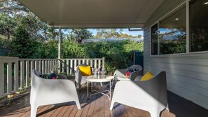 Un espace extérieur abrité, aménagé avec des chaises blanches et une table, entouré d’une terrasse en bois et d’une rambarde blanche.