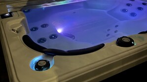 Un bain à remous doté de plusieurs jets et d’un panneau de commande, installé devant une clôture en bois.