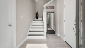 Un intérieur moderne avec un escalier, un panneau d’accueil et un miroir qui reflète le couloir.