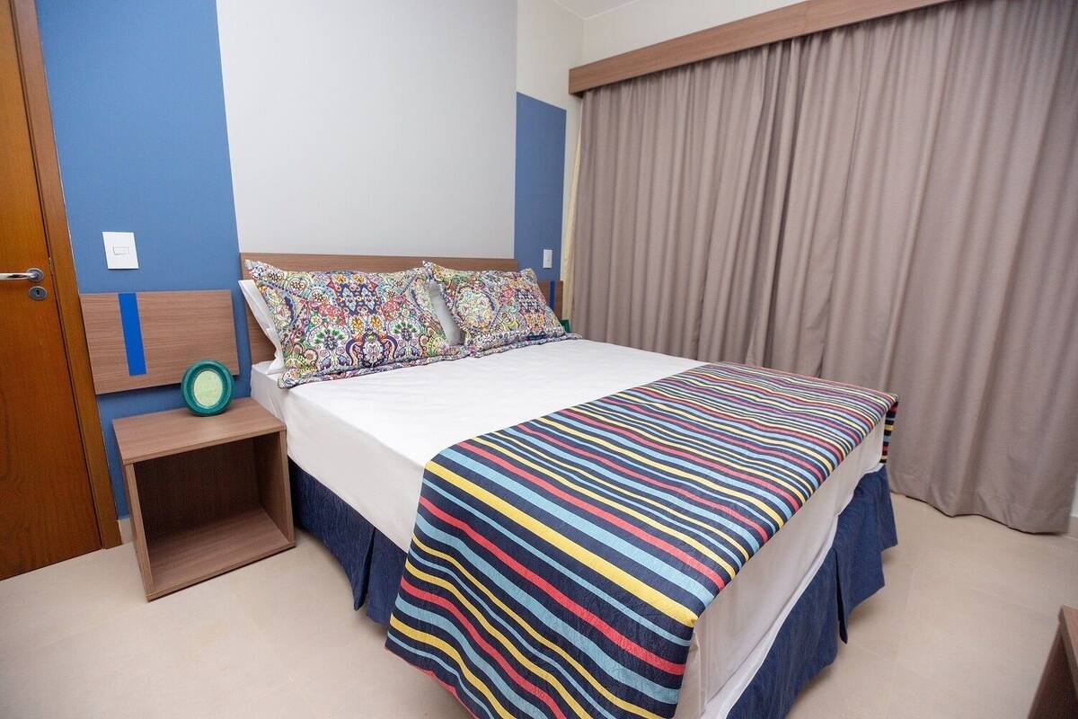 Un dormitorio con cama, mesita de noche, cómoda y ventana con cortinas.