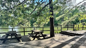 A wooden deck with picnic tables overlooking a body of water, surrounded by trees.