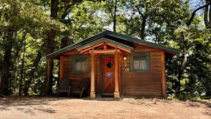 A rustic cabin with a wooden door, two windows, and a porch with chairs.