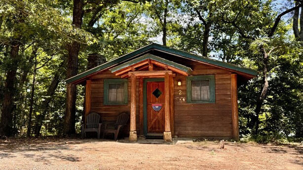 Eine rustikale Holzhütte mit einer Holztür, zwei Fenstern und einer Veranda mit Stühlen.