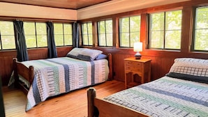 A room with two beds, wooden walls, and large windows.