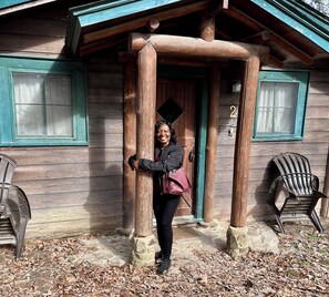 Une cabane en bois avec un porche, une porte portant un numéro et deux chaises à l’extérieur.