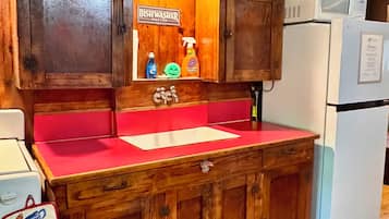 A wooden kitchen with a red countertop, a sink, cabinets, a dishwashing station, and a refrigerator.