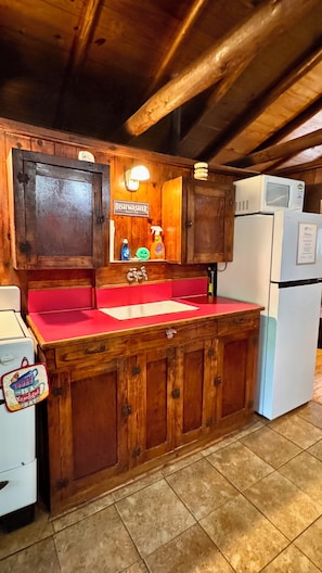 Una cocina de madera con cubierta roja, un lavabo, armarios, una estación para fregar platos y un refrigerador.