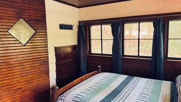 Un dormitorio con cabecera de madera, cama con colcha a rayas, mesita de noche y ventana con cortinas.